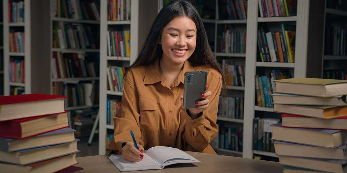 Estudante olhando seu celular na biblioteca - site colégio Equipe Belém - Pará