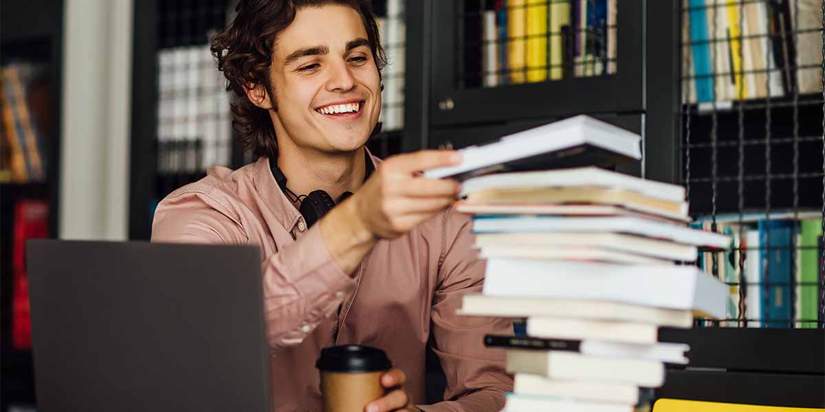 Rapaz na biblioteca empilhando livros - site Colégio Equipe - Belém - PA